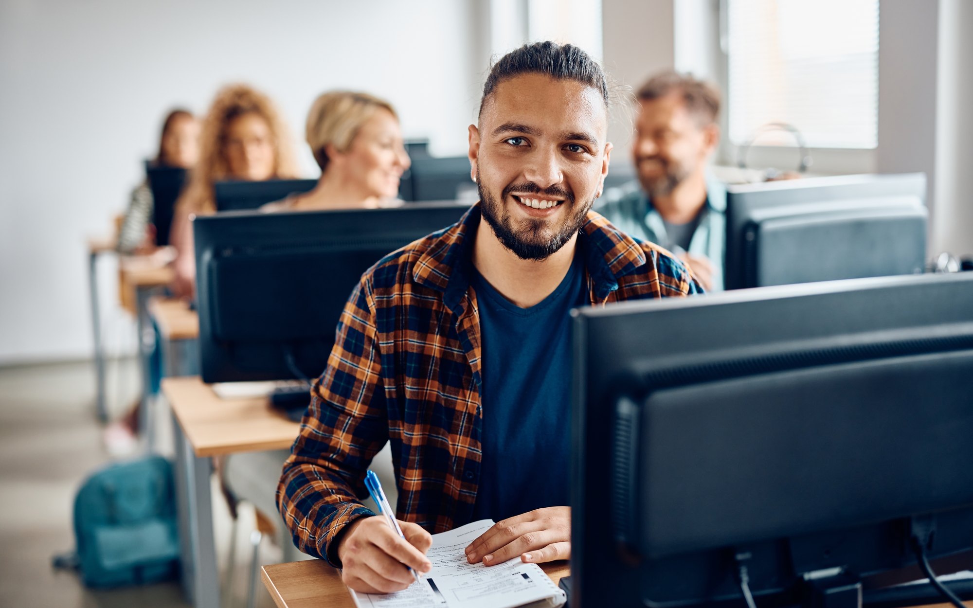 Students at workstations in a bright campus lab, one looking up from their notes